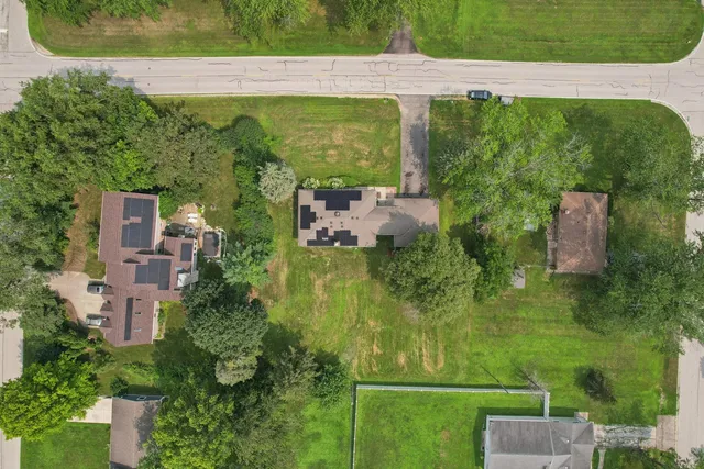 an aerial view of a residential houses with outdoor space and trees all around