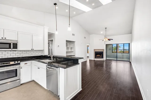 a kitchen with granite countertop a stove a sink a refrigerator and white cabinets with wooden floor