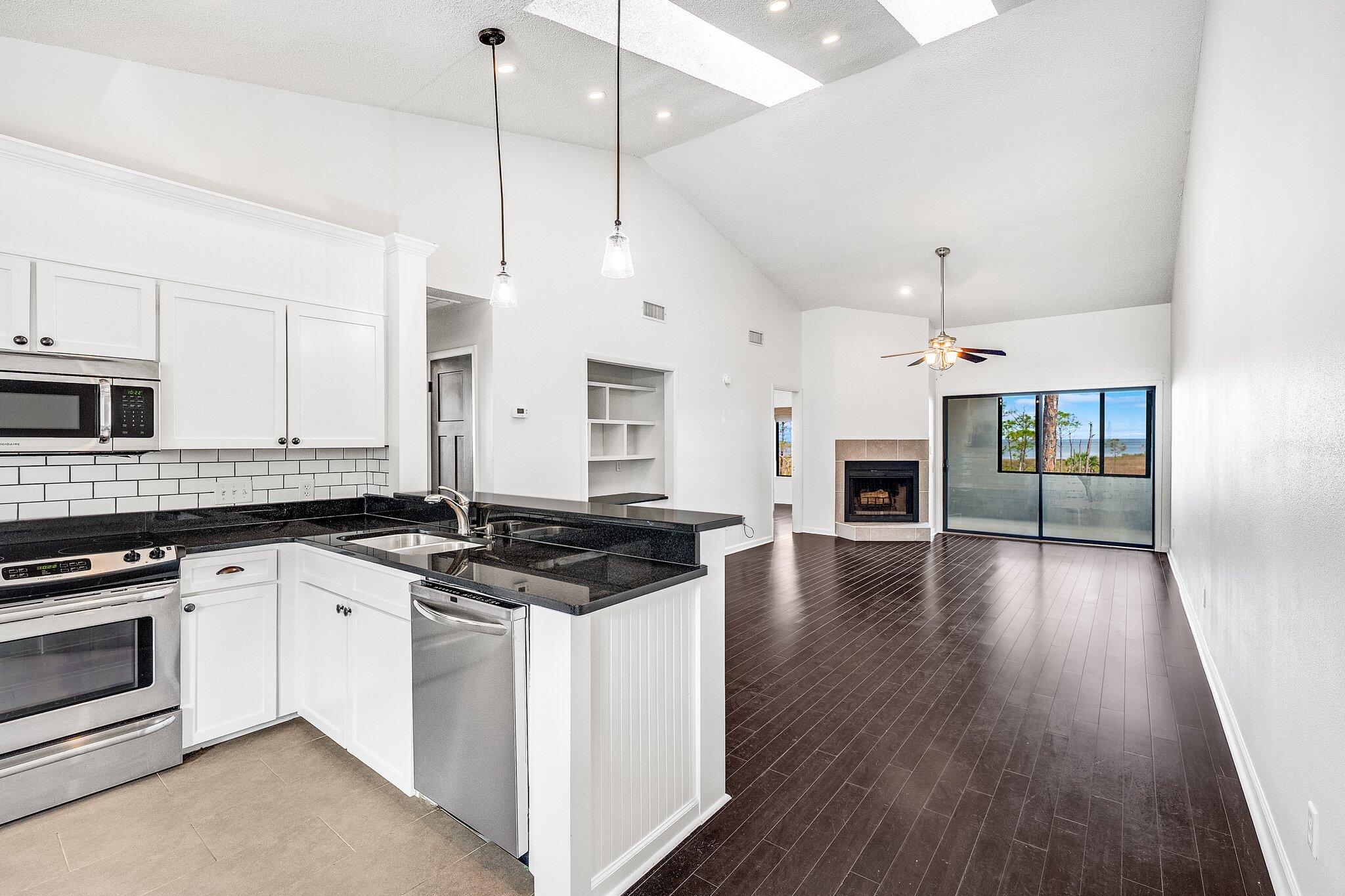 8983 Heron Walk Drive, Unit 8983 Miramar Beach, FL 32550 - Photo 4 of 57 a kitchen with granite countertop a stove a sink a refrigerator and white cabinets with wooden floor