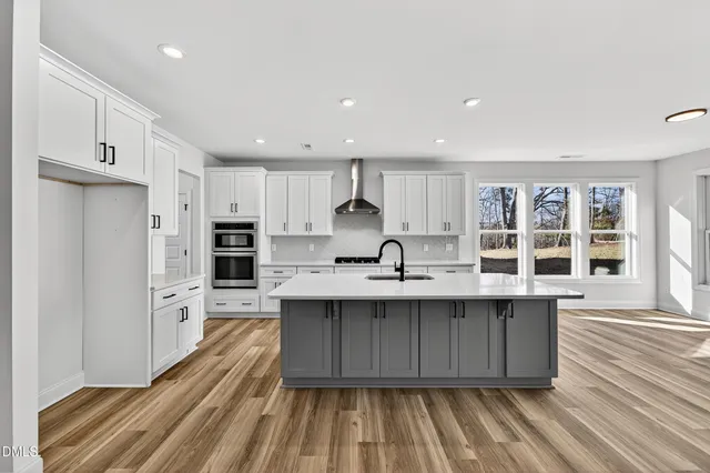 a kitchen with stainless steel appliances granite countertop a sink dishwasher a refrigerator and white cabinets with wooden floor