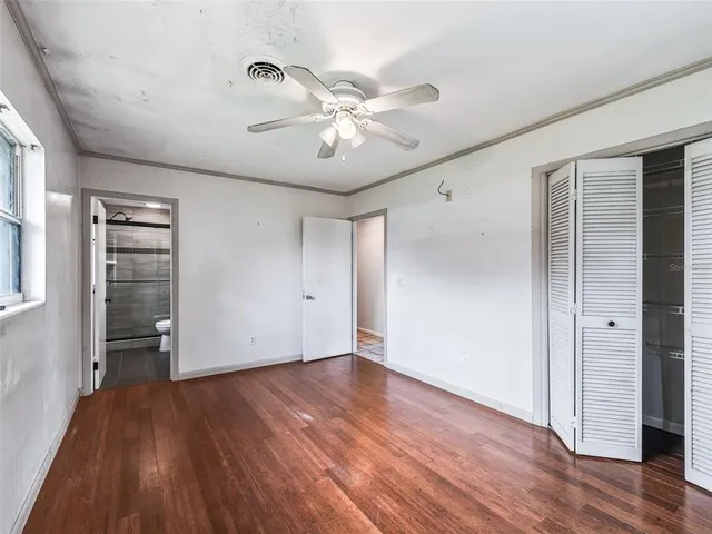 a view of an empty room with wooden floor and a ceiling fan