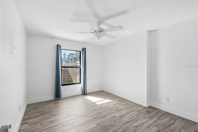 an empty room with wooden floor chandelier fan and windows
