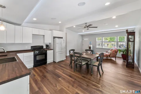 a kitchen with stainless steel appliances granite countertop a stove a refrigerator a kitchen island a dining table and chairs with wooden floor