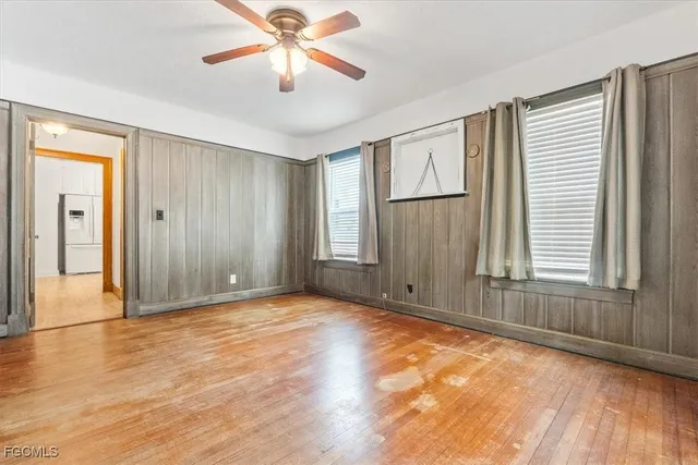 an empty room with wooden floor chandelier fan and windows