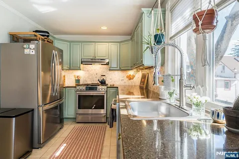 a kitchen with stainless steel appliances granite countertop a sink a stove a refrigerator cabinets and a window