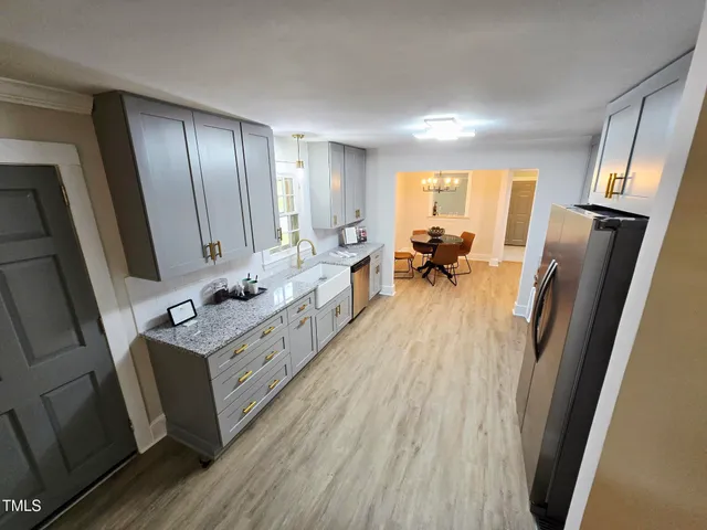 a large white kitchen with sink a refrigerator and wooden floor
