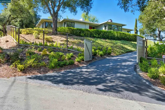 a view of a house with lots of plants and a table and chairs under an umbrella