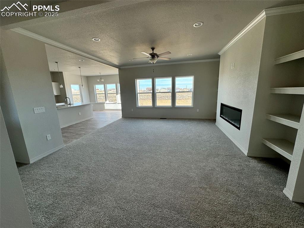 3955 Yoder Road Yoder, CO 80864 - Photo 6 of 27 Unfurnished living room with built in shelves, crown molding, carpet floors, a textured ceiling, and ceiling fan with notable chandelier