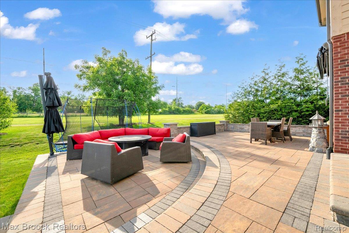 1126 Queensboro Drive Rochester, MI 48307 - Photo 45 of 66 Expansive paver patio with a curved stone retaining wall, brick exterior accents, and a wide grassy yard