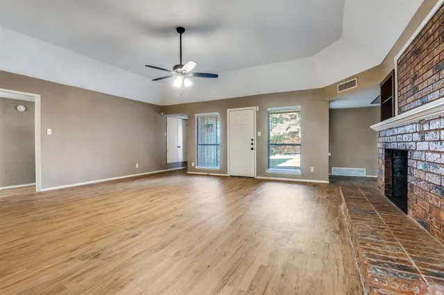 a view of an empty room with wooden floor fireplace and a window