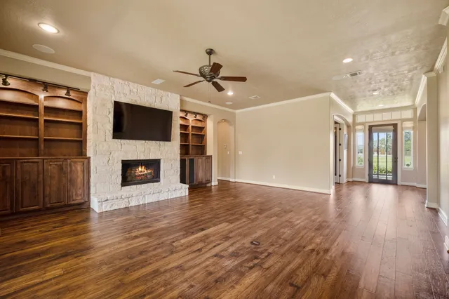 a view of a livingroom with a fireplace a ceiling fan and wooden floor