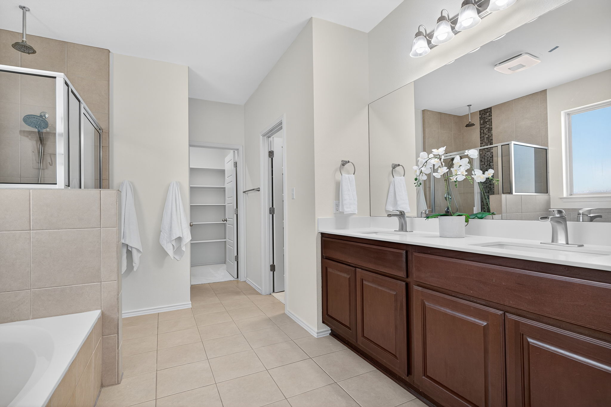 13300 Craven Lane Manor, TX 78653 - Photo 16 of 40 Primary bathroom featuring a walk-in shower, soaking tub, dual walk-in closets with built-in shelving, light tile patterned floors, and double vanity