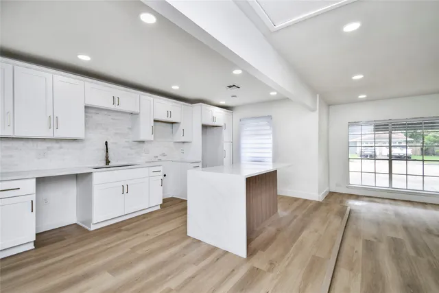 a large kitchen with stainless steel appliances granite countertop a stove a sink white cabinets and a wooden floor