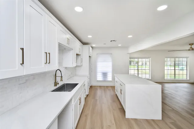 a large white kitchen with wooden floor and large window