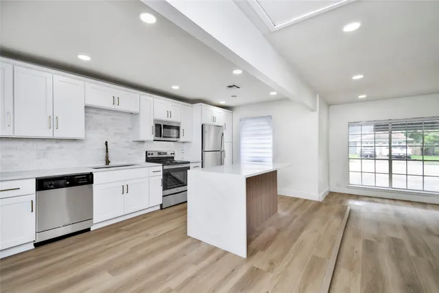 a large kitchen with stainless steel appliances granite countertop a stove a sink dishwasher and a oven with white cabinets