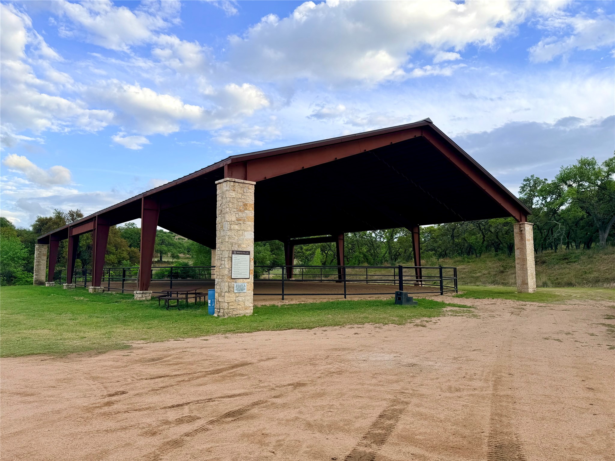 768 North Walnut Springs Road Johnson City, TX 78636 - Photo 21 of 22 Community amenity featuring a large covered arena with stone-clad columns and a sturdy metal roof, set within a natural landscape with trees