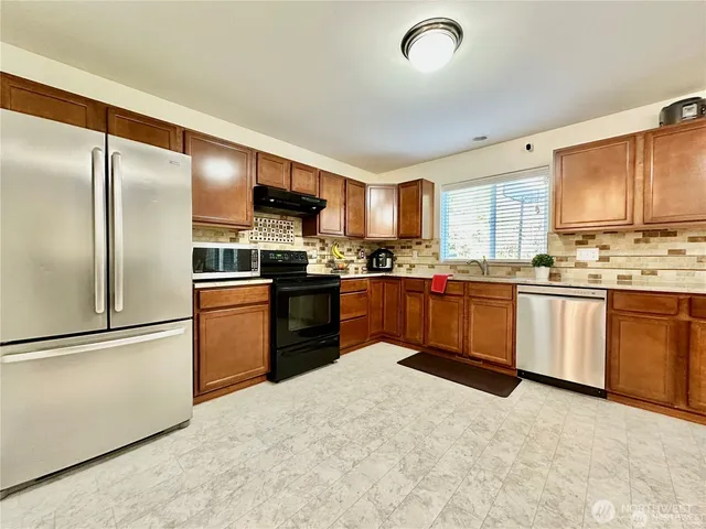 a kitchen with stainless steel appliances granite countertop a stove top oven a sink a refrigerator with white cabinets and a refrigerator