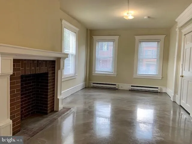an empty room with wooden floor fireplace and windows