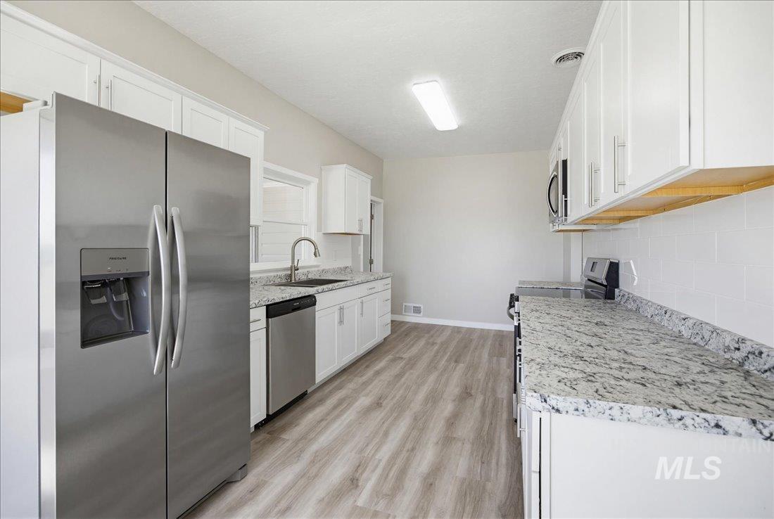 30013 Apple Valley Road Parma, ID 83660 - Photo 3 of 25 Kitchen featuring white cabinetry, light-toned wood-finish flooring, stainless steel appliances, speckled countertops, and a white subway tile backsplash