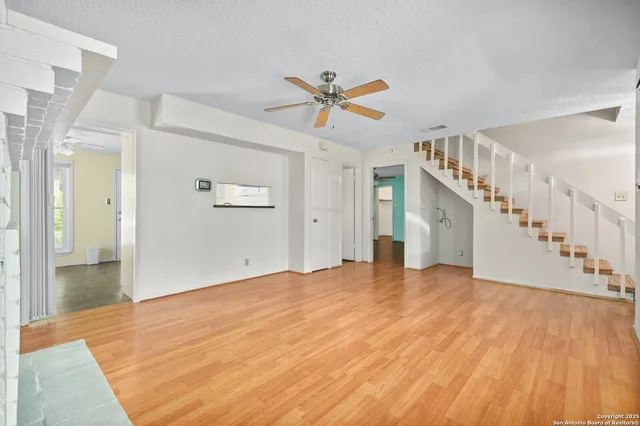 a view of an empty room with wooden floor and a ceiling fan