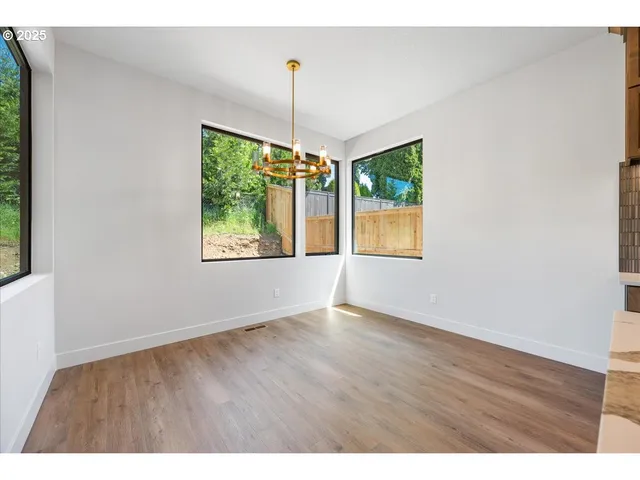 a view of an empty room with wooden floor ceiling fan and window