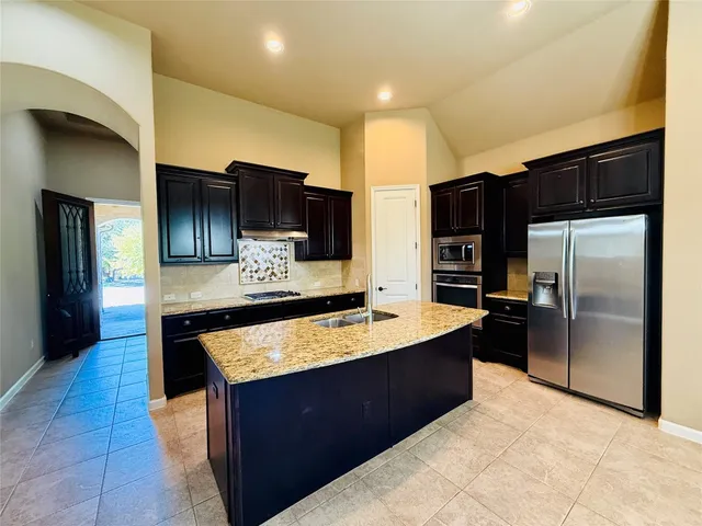 a large kitchen with stainless steel appliances kitchen island granite countertop a refrigerator and a sink