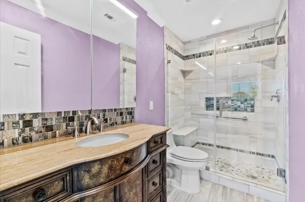 a bathroom with a granite countertop sink a toilet a mirror and shower