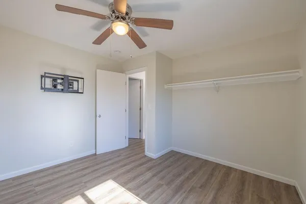 an empty room with wooden floor ceiling fan and window