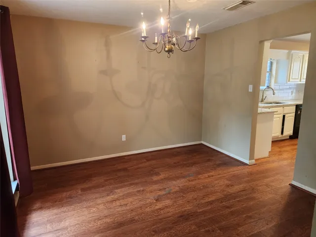a view of an empty room with wooden floor and a kitchen