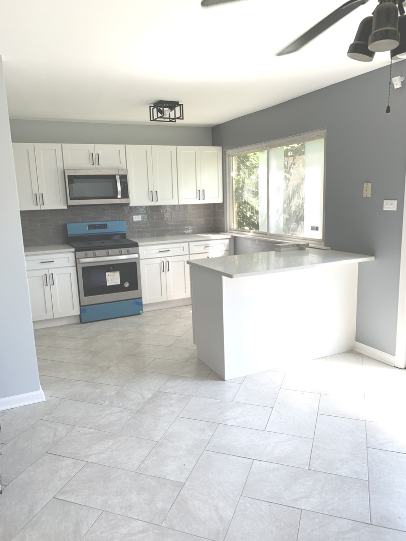 74 West 140th Street Riverdale, IL 60827 - Photo 4 of 20 a large kitchen with a stove a sink a microwave and glass cabinets