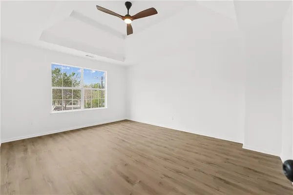 an empty room with wooden floor ceiling fan and windows