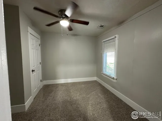 an empty room with chandelier fan and windows