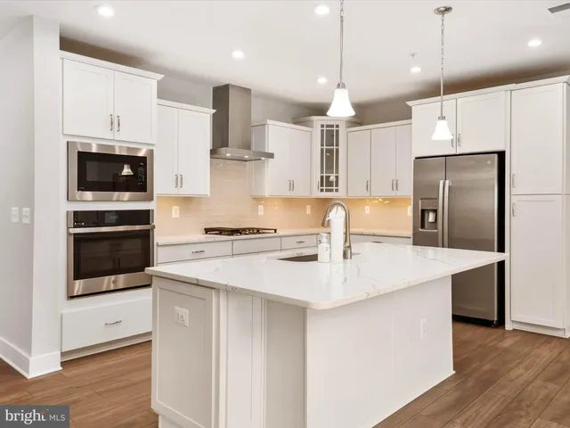 a view of an empty room with wooden floor and kitchen space