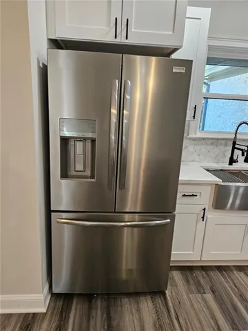 a view of a refrigerator in kitchen and an empty room with wooden floor