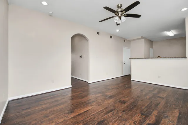 a view of an empty room with wooden floor and a ceiling fan