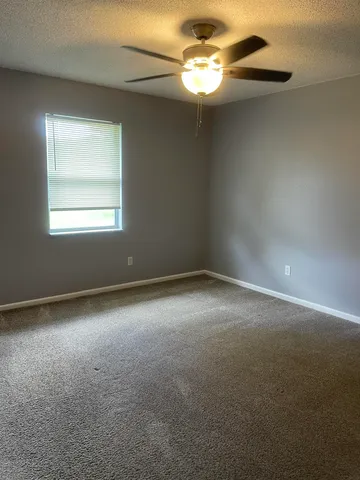 an empty room with a chandelier fan and windows
