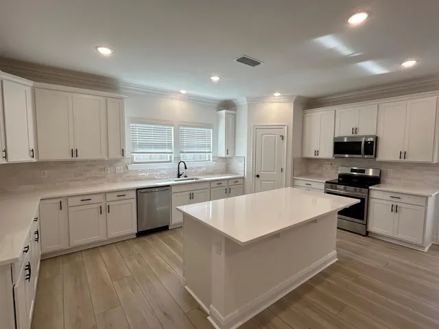 a large kitchen with kitchen island a sink dishwasher stove and white cabinets with wooden floor