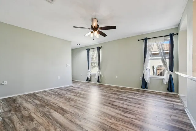 a view of a room with wooden floor ceiling fan and windows