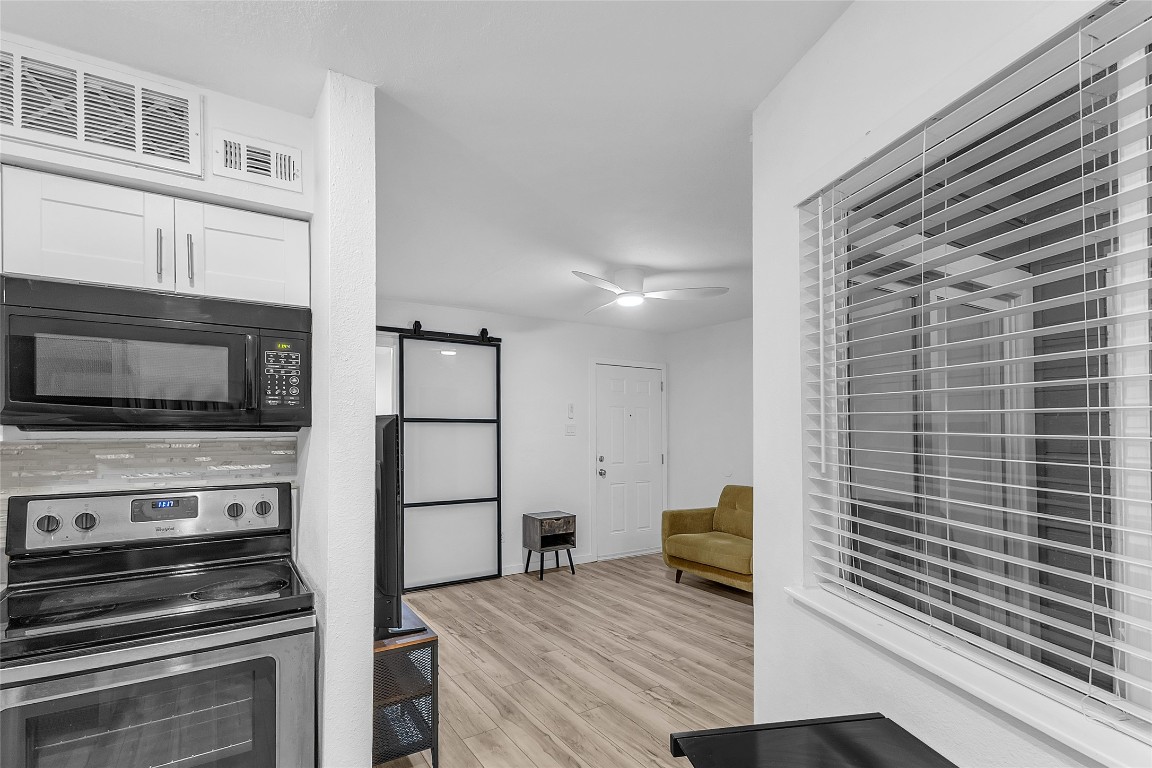 1840 Burton Drive, Unit 184 Austin, TX 78741 - Photo 3 of 23 Kitchen featuring a barn door, stainless steel electric range, black microwave, light wood-type flooring, and white cabinets