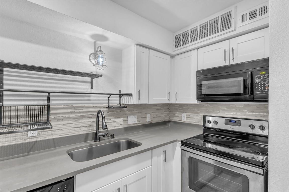 1840 Burton Drive, Unit 184 Austin, TX 78741 - Photo 5 of 23 Kitchen with stainless steel electric range, backsplash, white cabinets, black microwave, and light stone counters