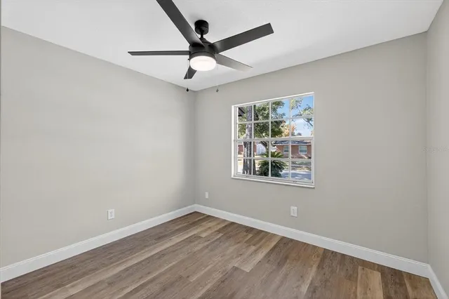 an empty room with wooden floor ceiling fan and windows