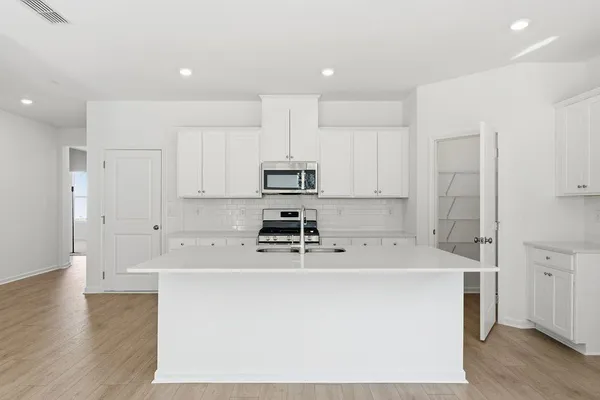 a kitchen with stainless steel appliances a sink a stove a refrigerator cabinets and a wooden floor