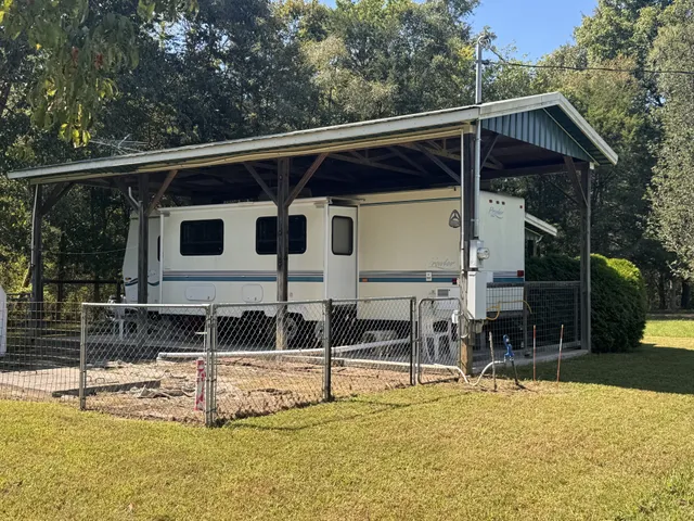 a view of a patio with a table and chairs under an umbrella with large trees