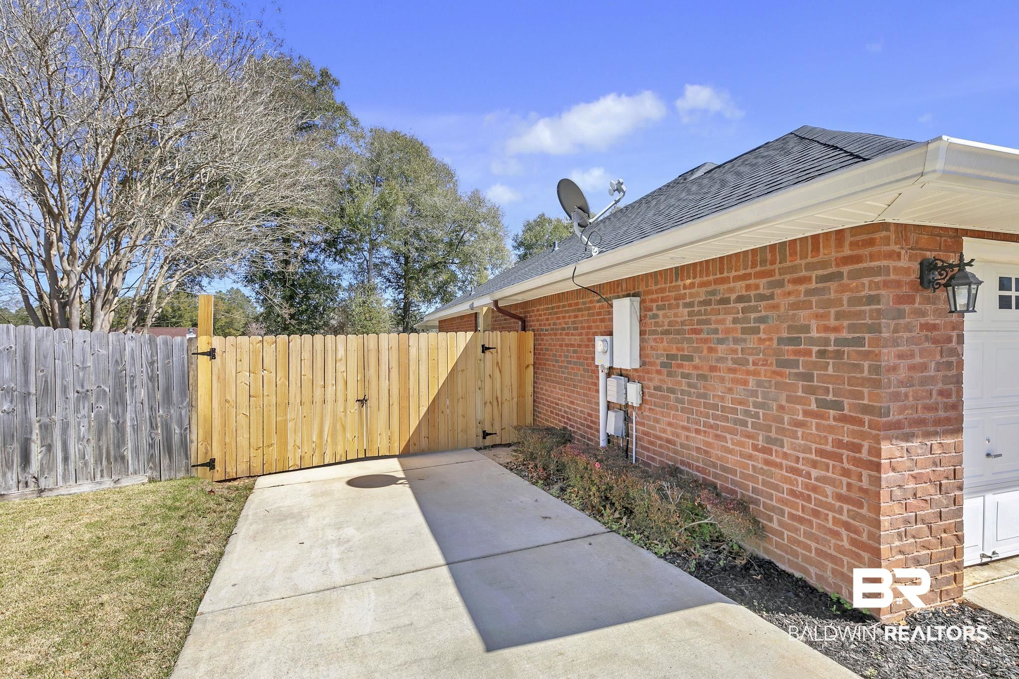 11103 Pontchartrain Loop Daphne, AL 36526 - Photo 26 of 29 View of side of home with brick siding, a shingled roof, fence, and a gate