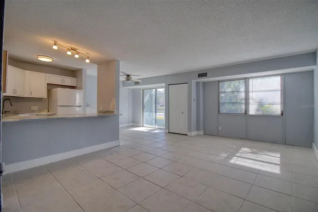 a view of an empty room with kitchen and window