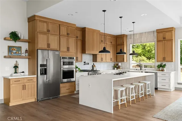 a kitchen with stainless steel appliances granite countertop a refrigerator a sink dishwasher a stove and a dining table with wooden floor