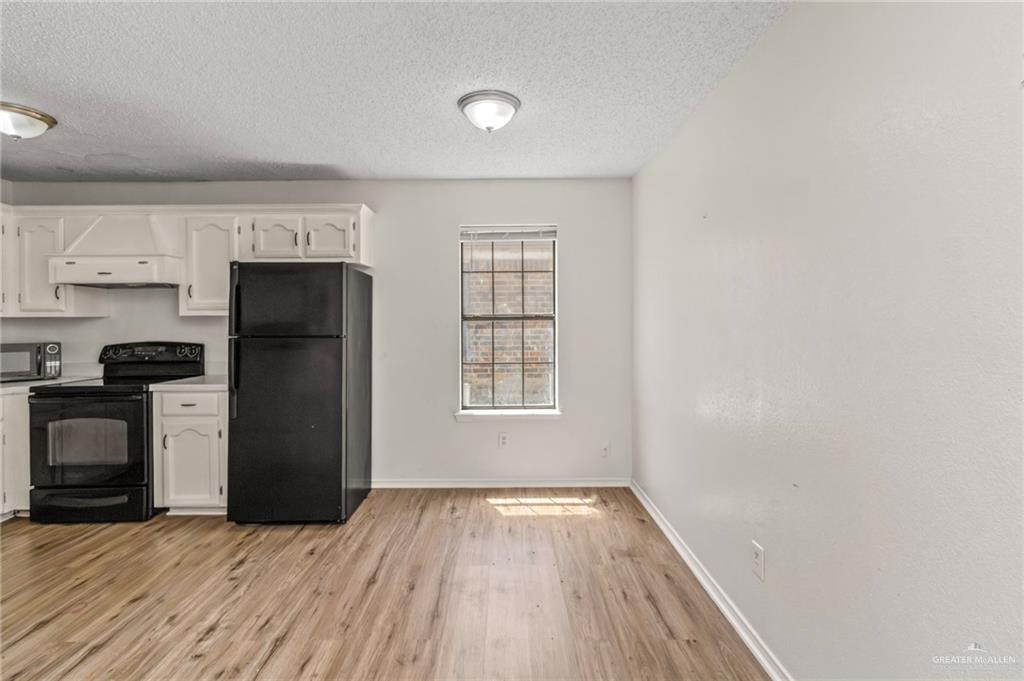 4601 South 24th Street, Unit 3 McAllen, TX 78503 - Photo 4 of 9 Kitchen with black appliances, white cabinetry, exhaust hood, a textured ceiling, and light wood-style flooring