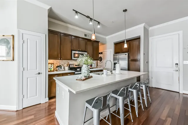 a kitchen with stainless steel appliances a stove top oven a sink dishwasher a dining table and chairs with wooden floor