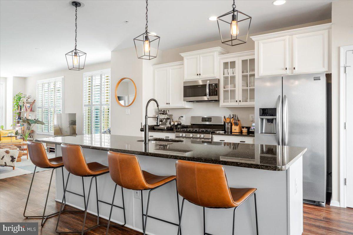 6500 Newton Drive Frederick, MD 21703 - Photo 3 of 36 a kitchen with stainless steel appliances granite countertop a stove a refrigerator a kitchen island a sink dishwasher a dining table and chairs with wooden floor