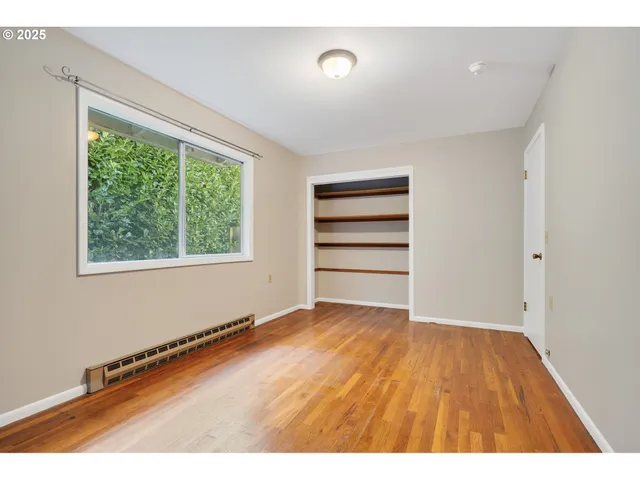 a view of an empty room with a window and wooden floor